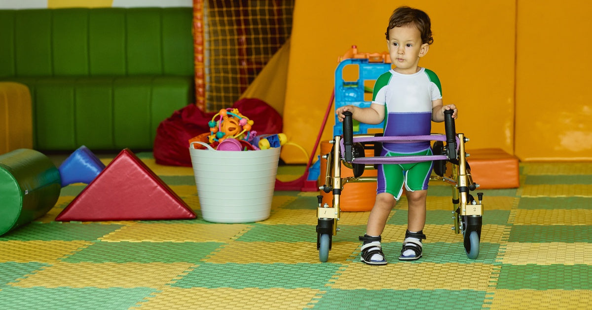 A young child using a pediatric mobility walker to stand in a colorfully decorated rehabilitation clinic.