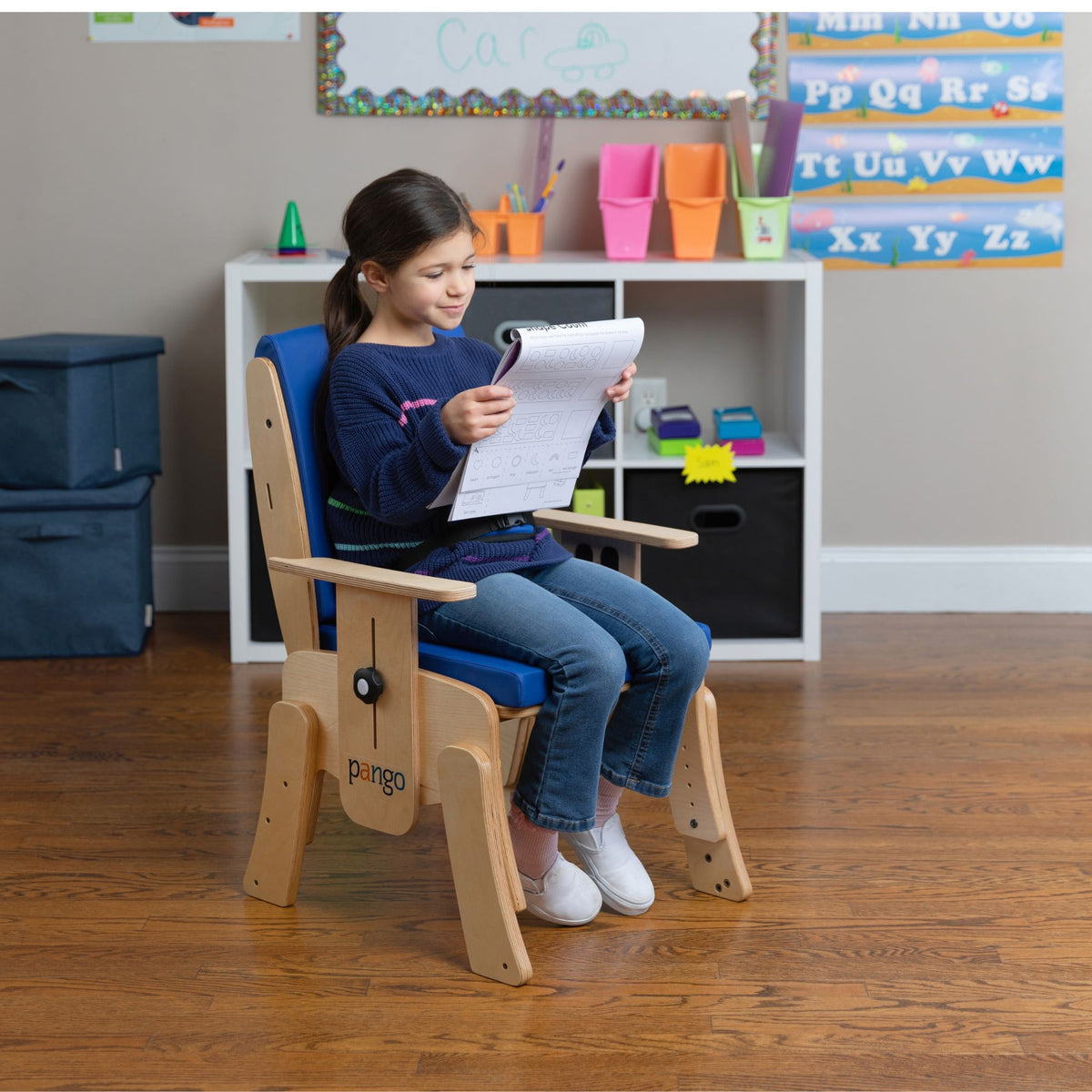 Young girl reading a worksheet while seated in a blue Circle Specialty Pango school chair with pelvic belt in a classroom