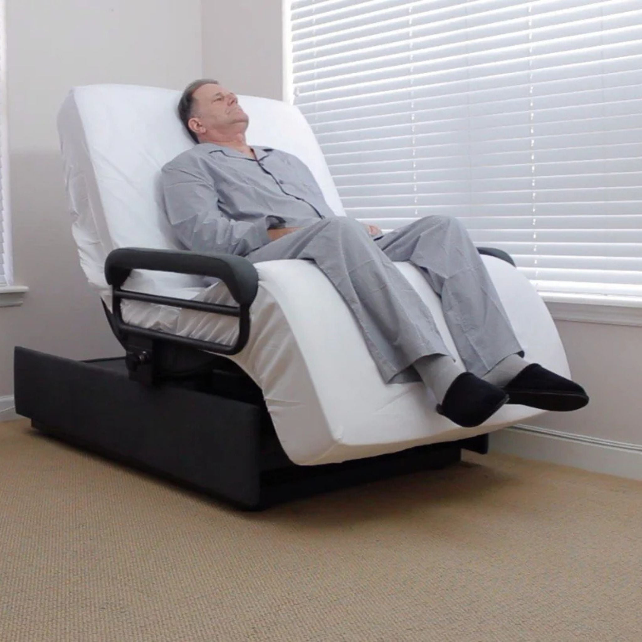 User relaxing in the ENVYY Sleep-to-Stand adjustable bed by Platinum Health in a reclined comfort position with elevated backrest, ergonomic leg support, and padded safety rails designed for homecare and aging-in-place comfort.