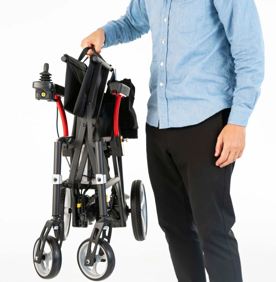 Man lifting the folded 33 pound Feather Power Chair by its handle with one hand