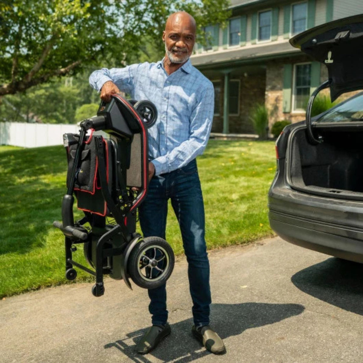 Man carrying the folded 37 pound Feather Scooter with one hand beside an open car trunk