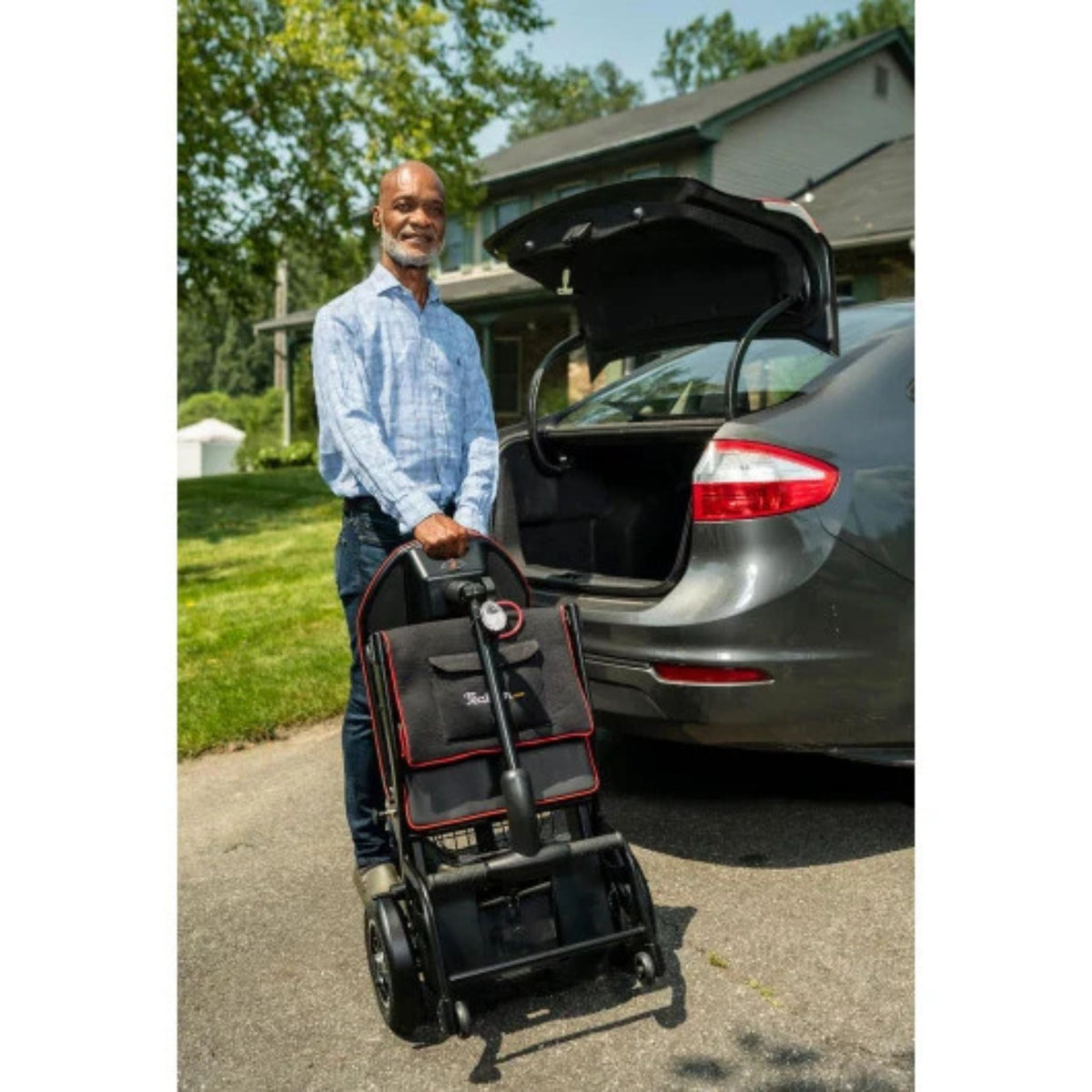 Man standing beside an open car trunk holding the folded Feather Scooter upright by its carry handle