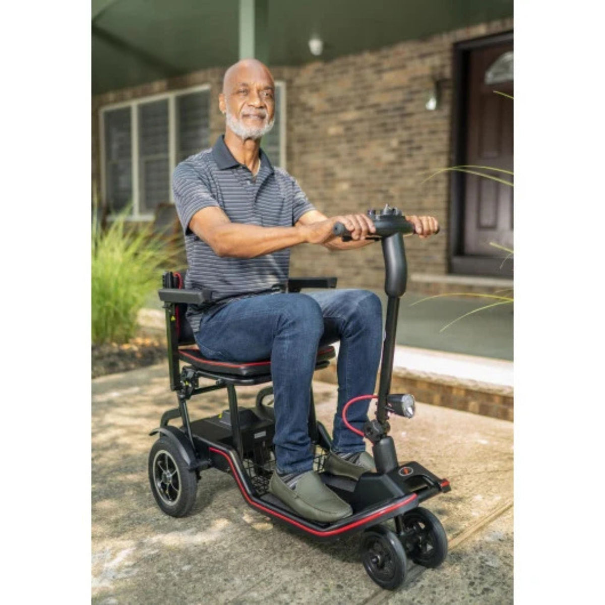 Man seated on the Feather Scooter on a front walkway with his hands on the tiller