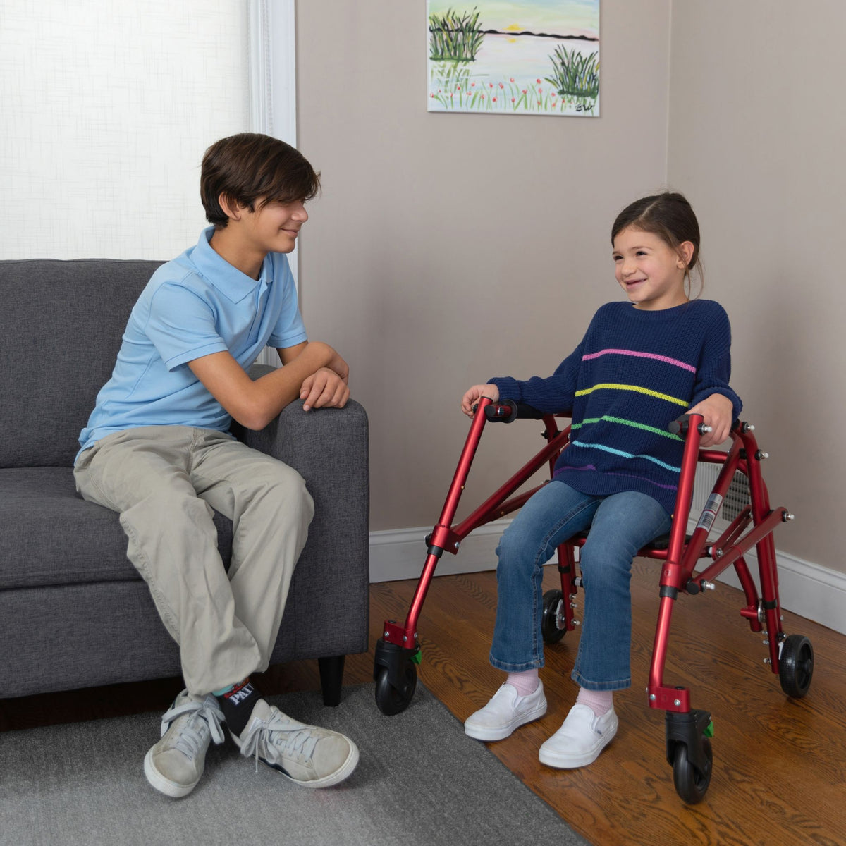 Girl resting on the flip-up seat of a red Klip posterior walker while talking with her brother