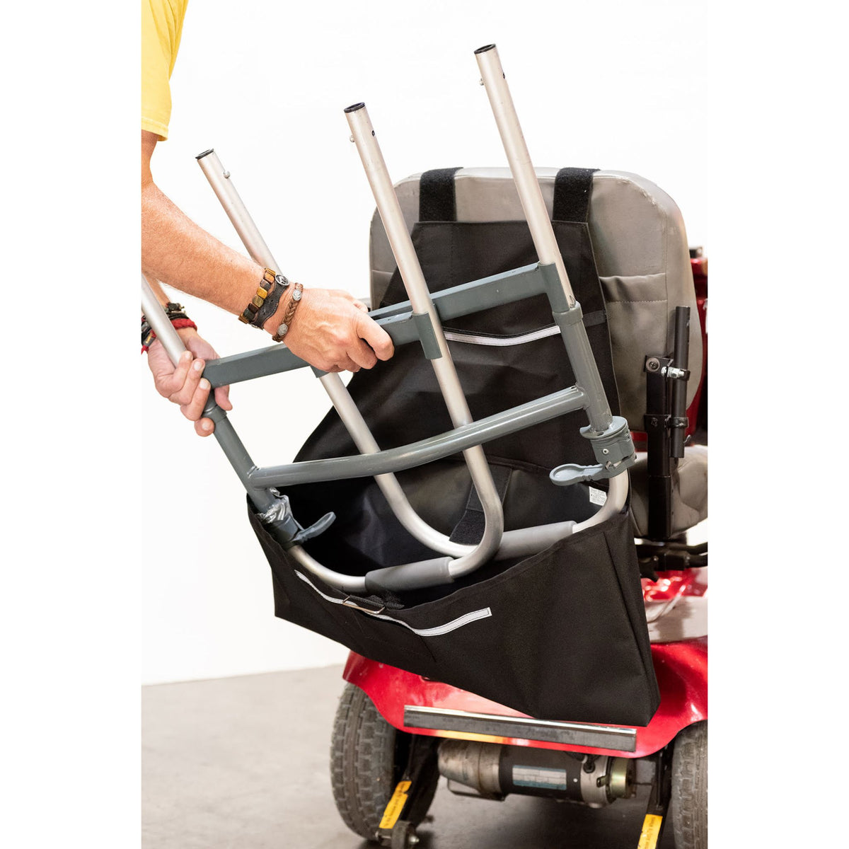 Person lowering a folded walker into the Diestco Walker Holder pouch behind a mobility scooter seat