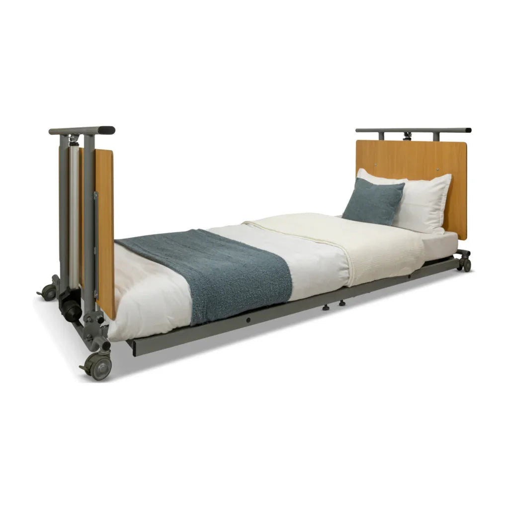 Low profile medical bed with wood headboard, white bedding and blue blanket, on wheels