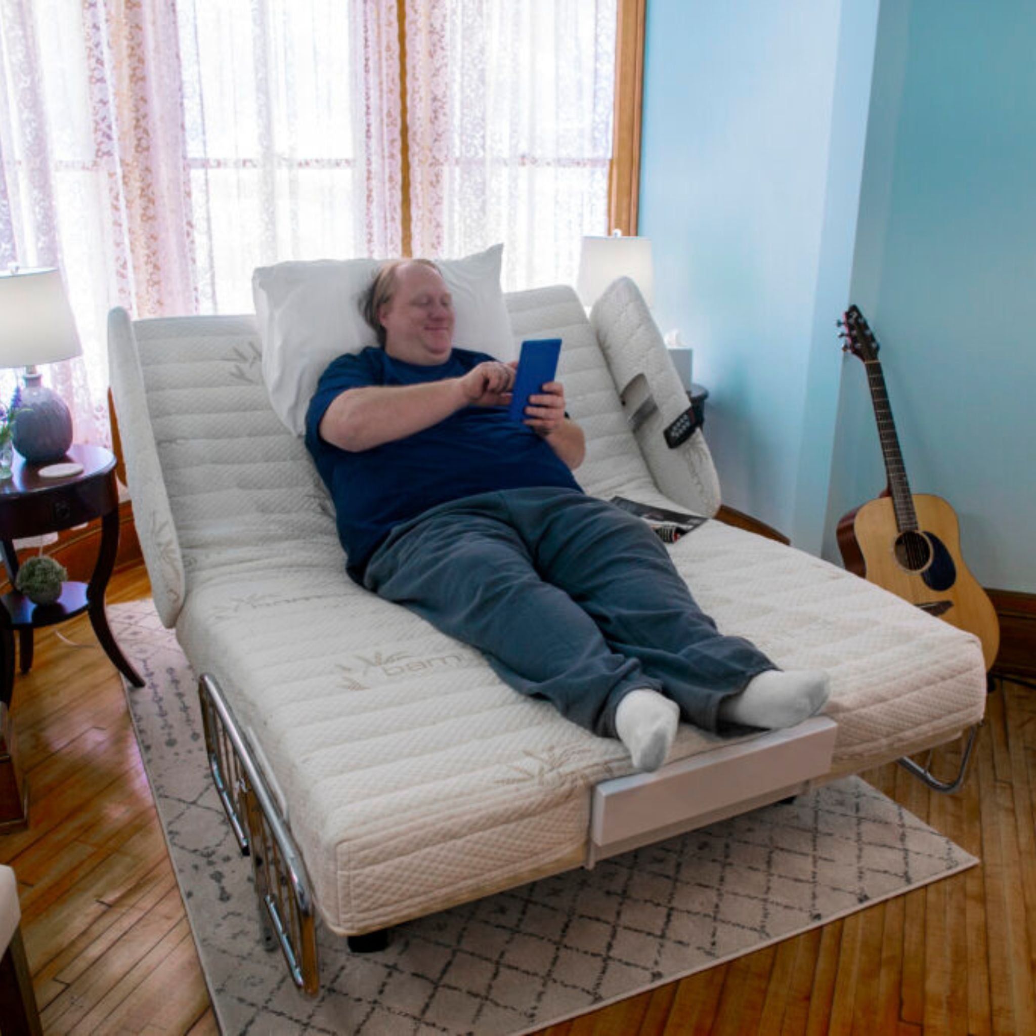 Man reclining comfortably on a Night Rider HD bariatric bed with the head raised, reading in a home bedroom