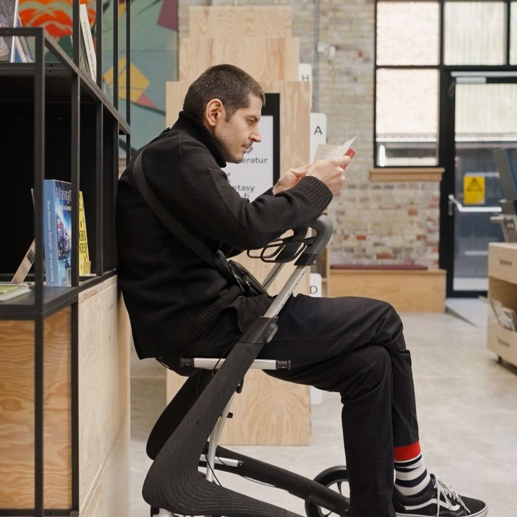 Man seated on the built-in seat of a byACRE Nordic Pioneer rollator reading indoors