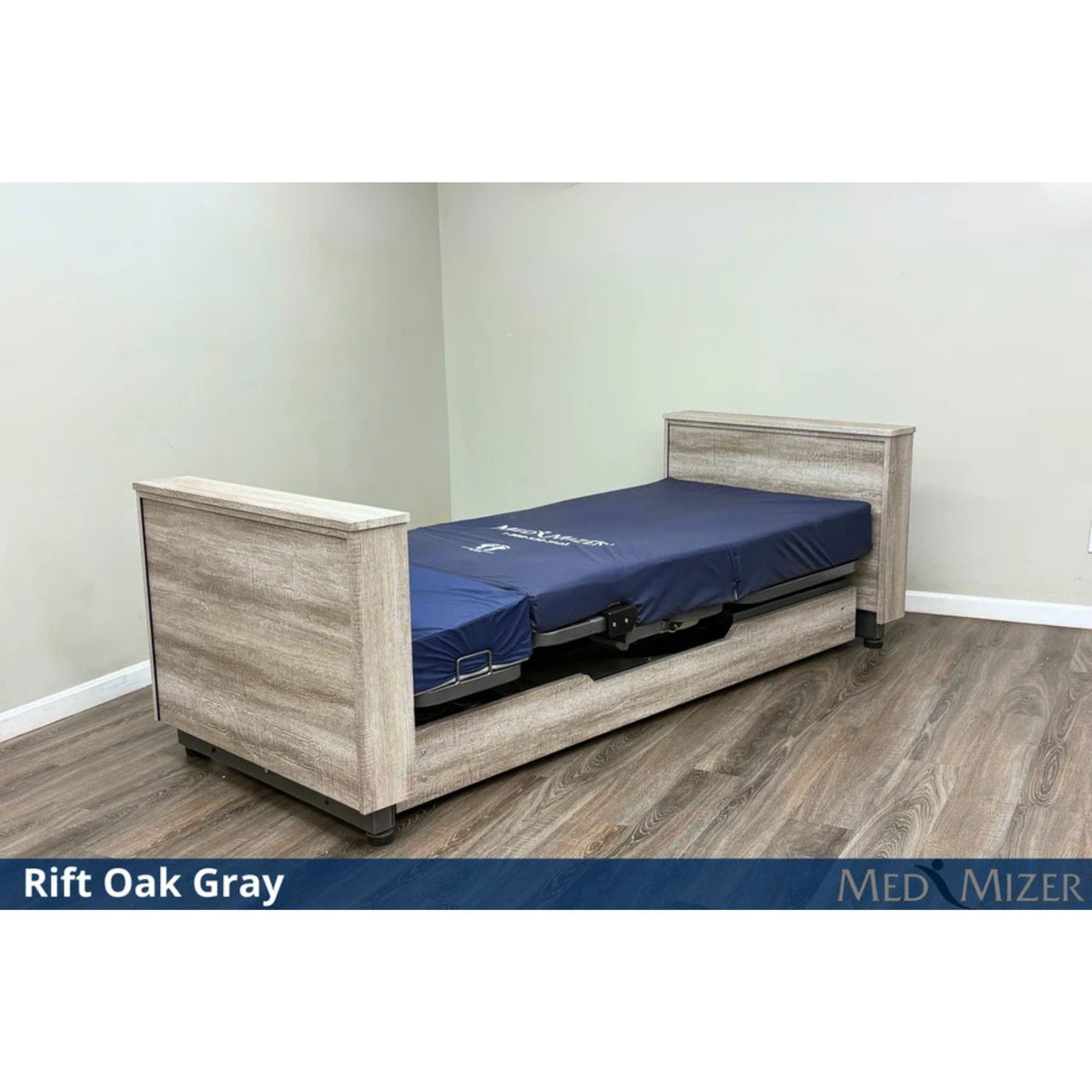Med-Mizer ActiveCare Deluxe rotating pivot home care bed in Rift Oak Gray, lowered flat with a blue mattress