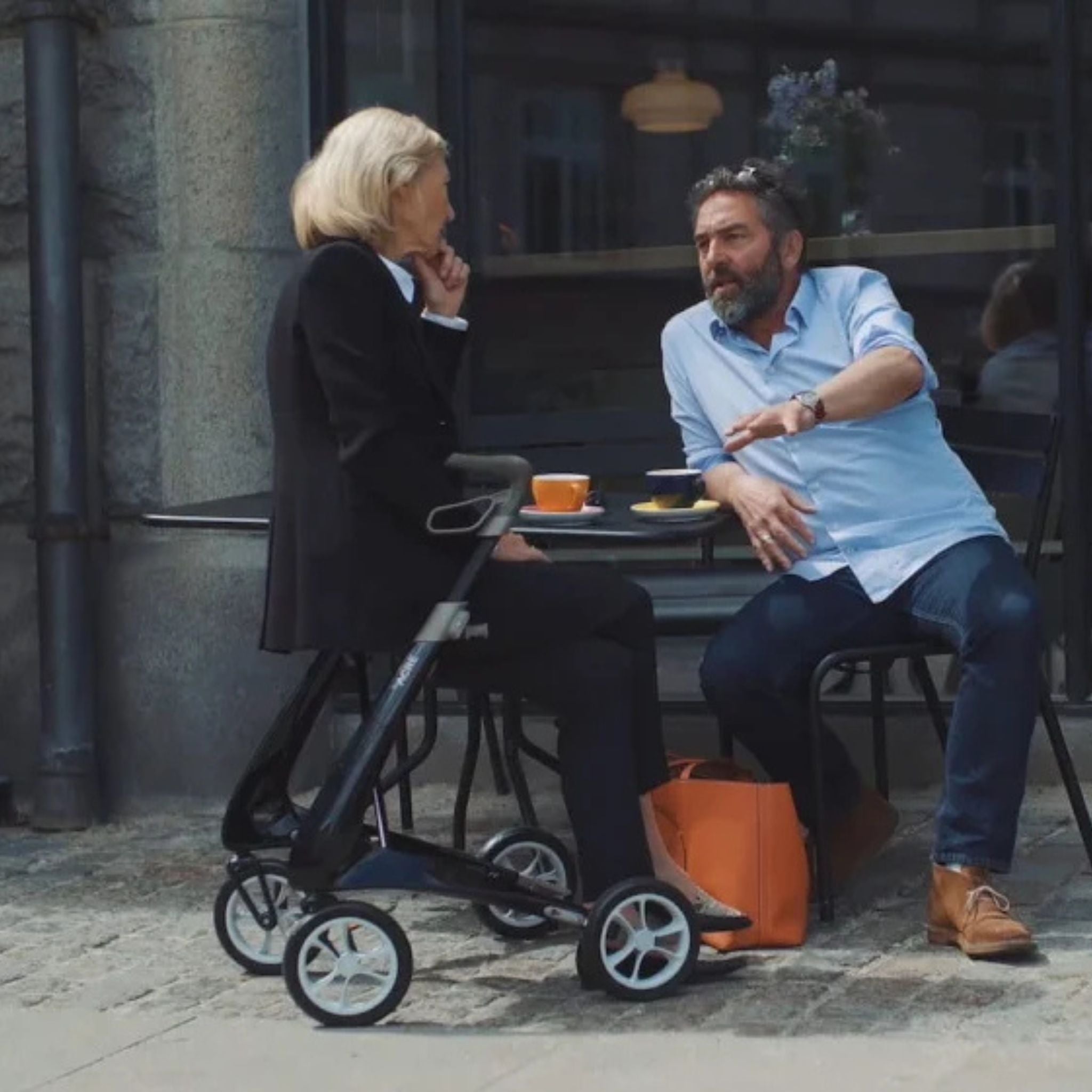 Woman using a Carbon Black byACRE Carbon Ultralight rollator with seat at an outdoor café table
