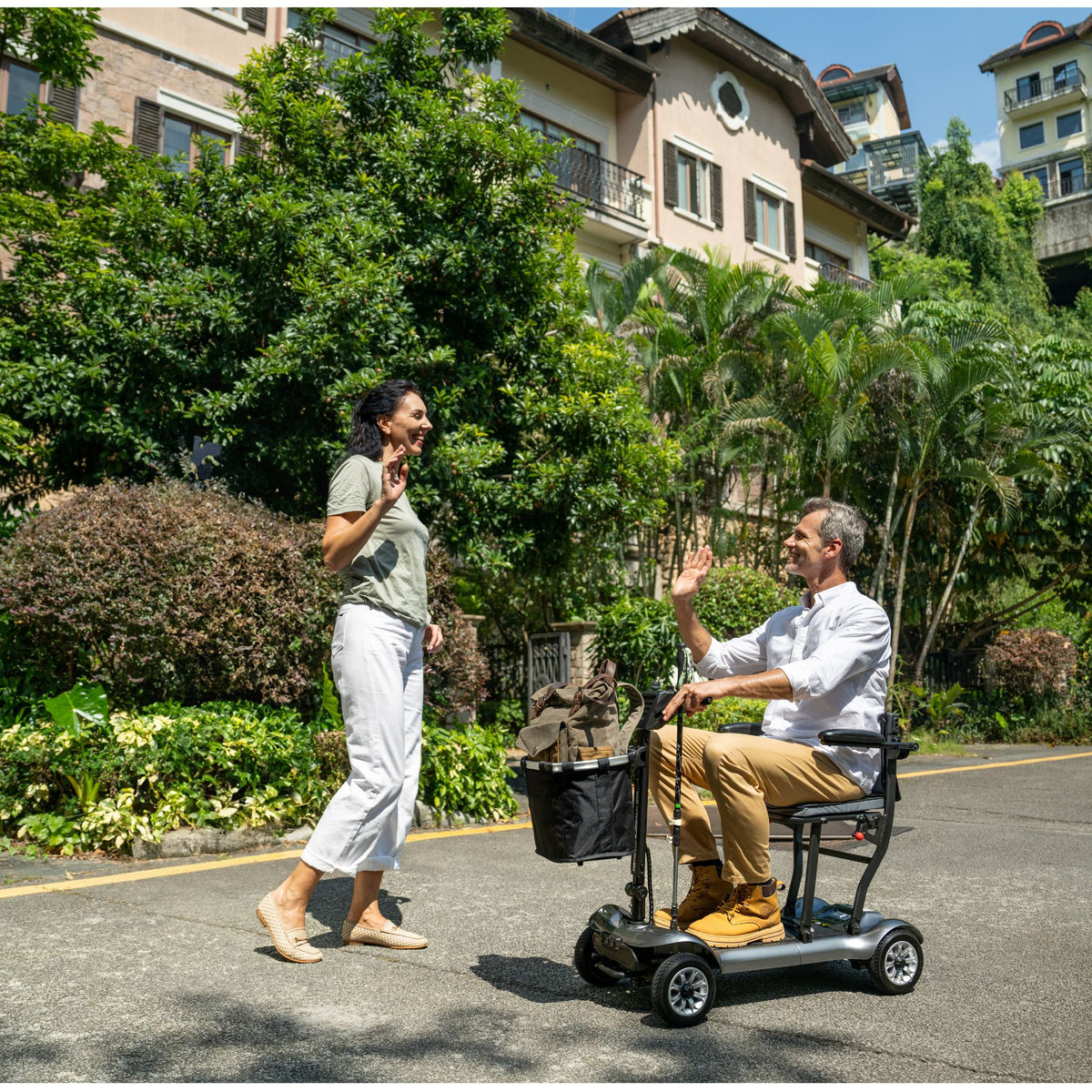 Man on a gray Paiseec D3 mobility scooter waving to a friend on a tree-lined neighborhood street