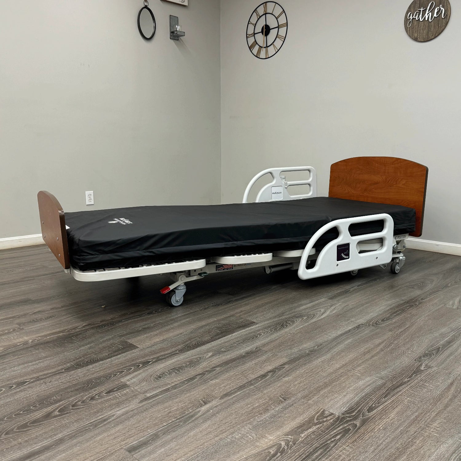Hospital bed in a room with wooden flooring and gray walls.