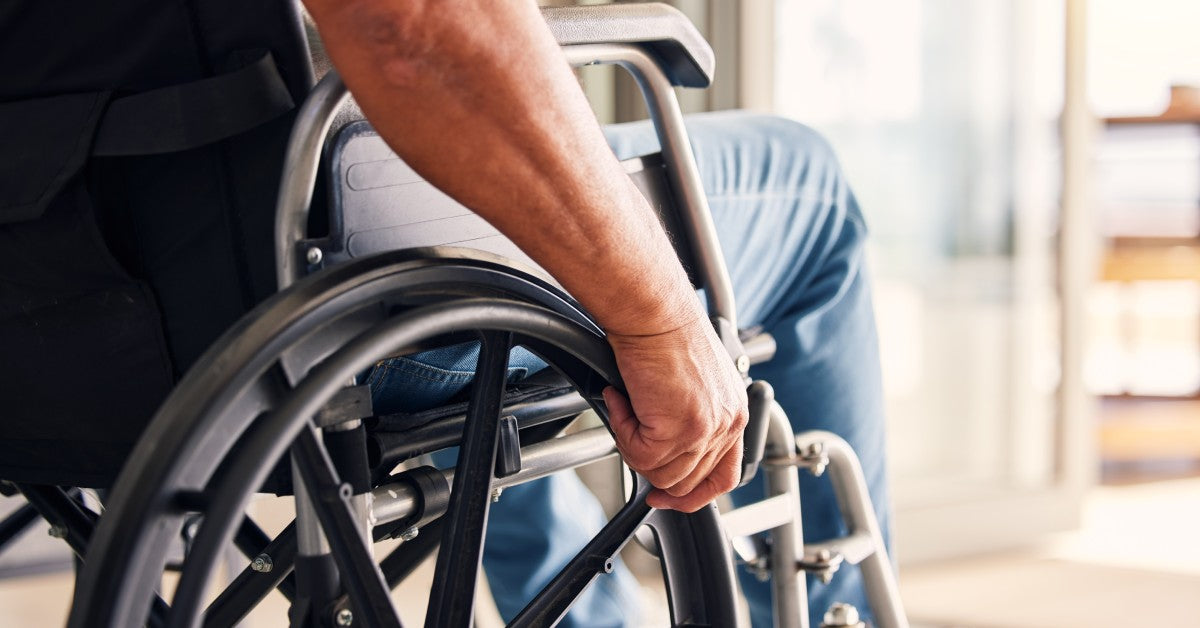 A person sitting in a wheelchair in front of an open door. Warm sunlight streams into the room through the doorway.