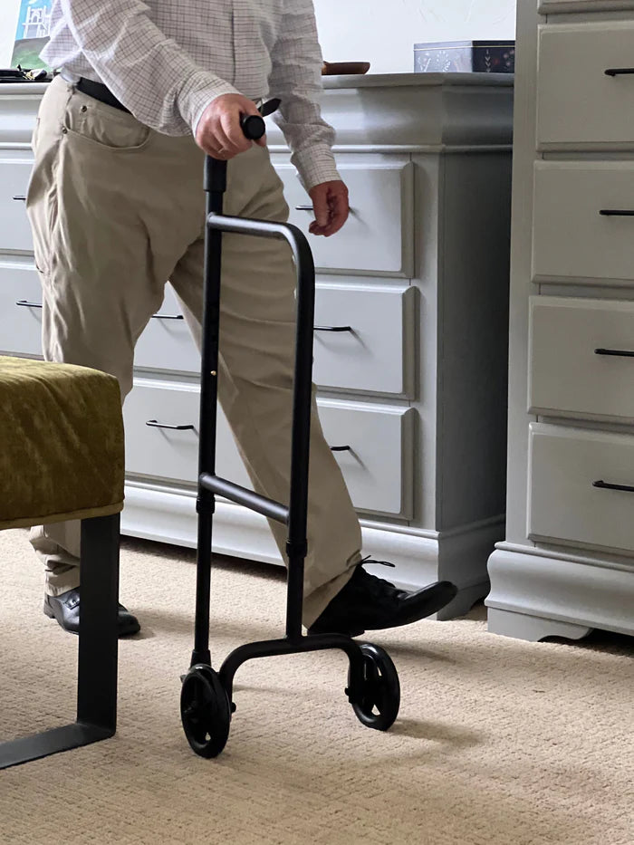 Person using a black walker in a room with white cabinets.