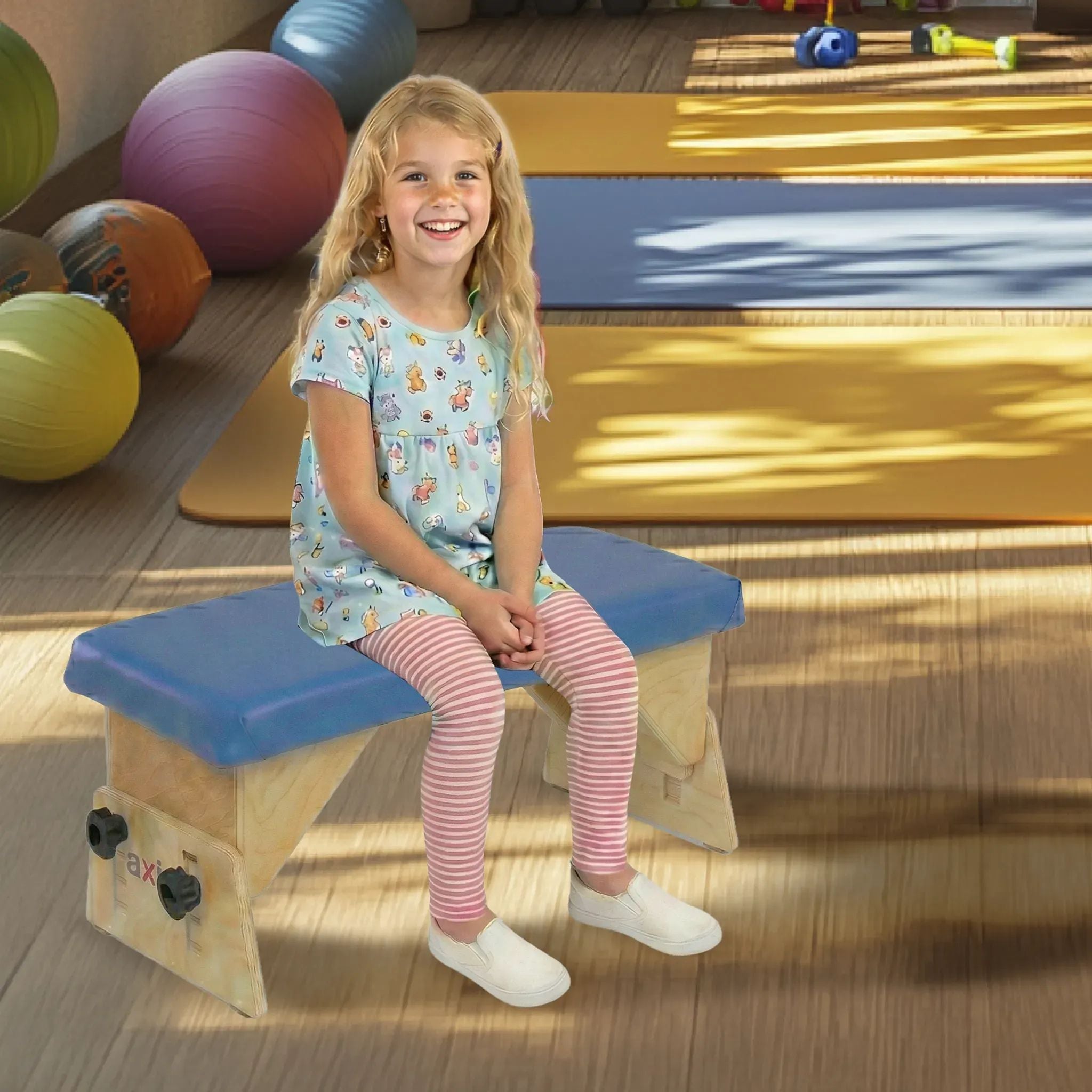 Little girl seated with feet flat on adjustable Axis therapy bench in a pediatric therapy gym