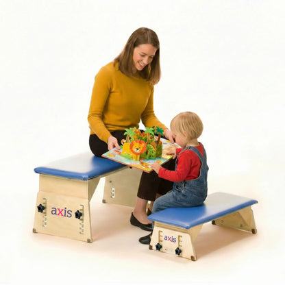 Caregiver reading a pop-up book with a toddler, each seated on a different size Axis therapy bench