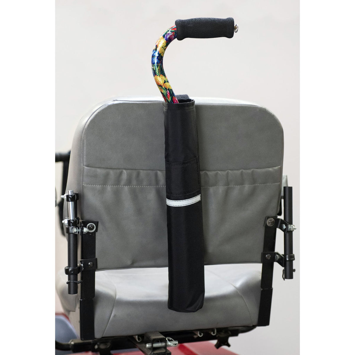 Diestco Cane Holder strapped to a power wheelchair seatback with hook-and-loop, holding an offset cane upright behind the headrest