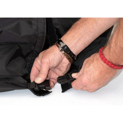 Hands fastening the side-release buckle at the bottom of the Diestco wheelchair cover’s hook-and-loop back slit
