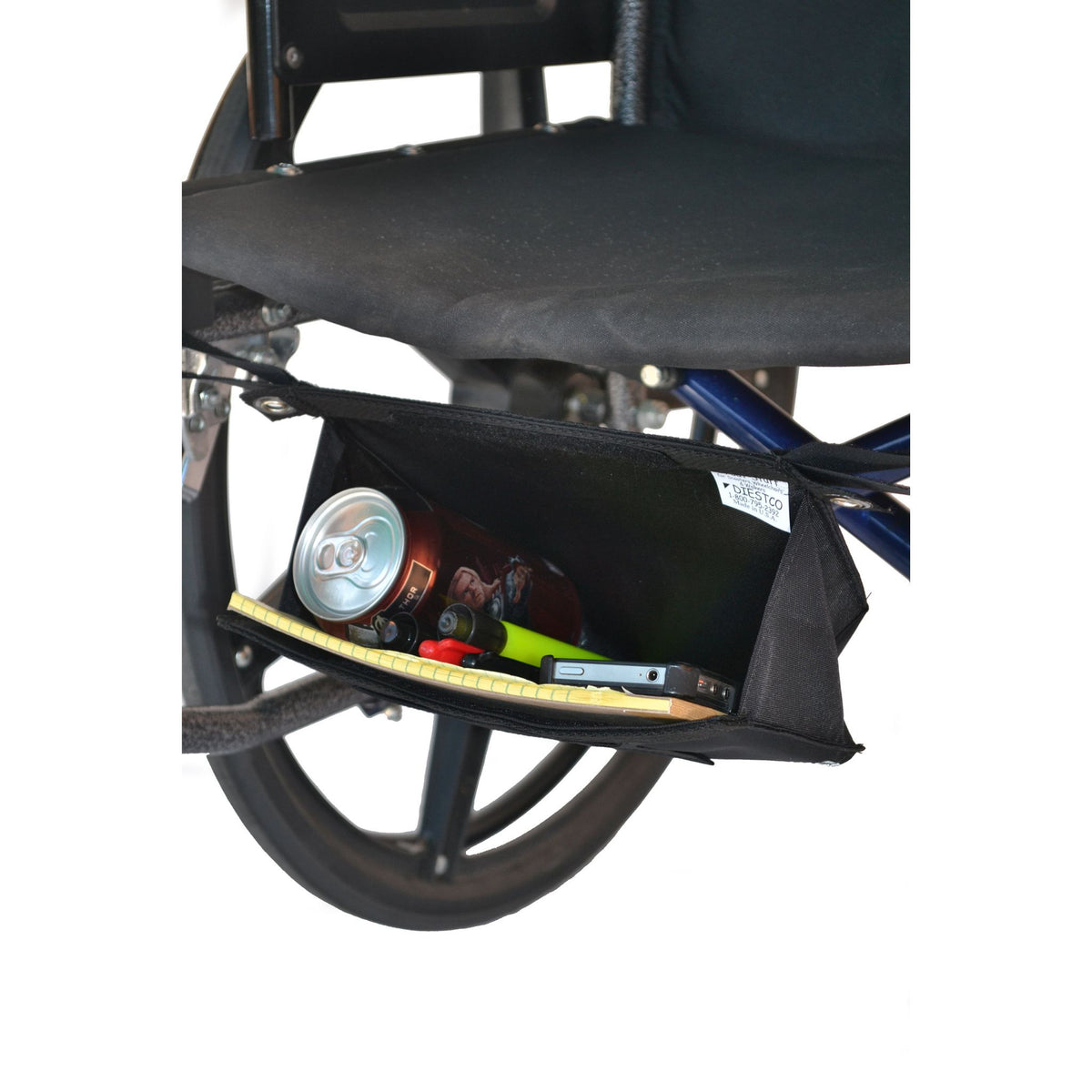 Angled view of the Diestco Small Glove Box mounted beneath a manual wheelchair seat, open with a can, notepad, and phone inside