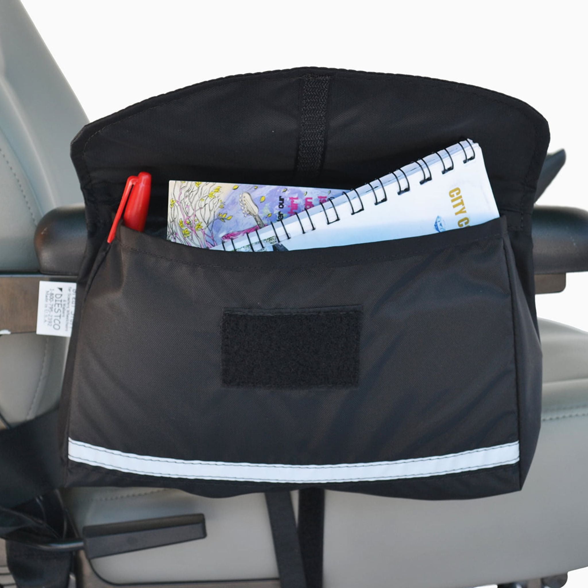 Diestco Standard Saddle Bag on a wheelchair armrest holding a notebook and pen, with an ID pocket and reflective strip