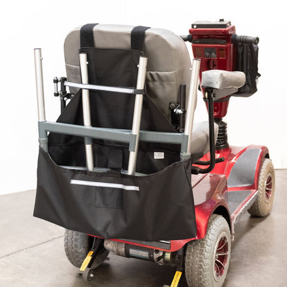 Diestco Walker Holder strapped to a mobility scooter seatback, carrying a folded four-post walker upright behind the seat, with reflective strips
