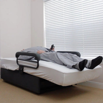 User resting in the ENVYY Sleep-to-Stand adjustable bed by Platinum Health in a flat sleeping position with supportive padded safety rails and remote-controlled positioning in a home bedroom environment.