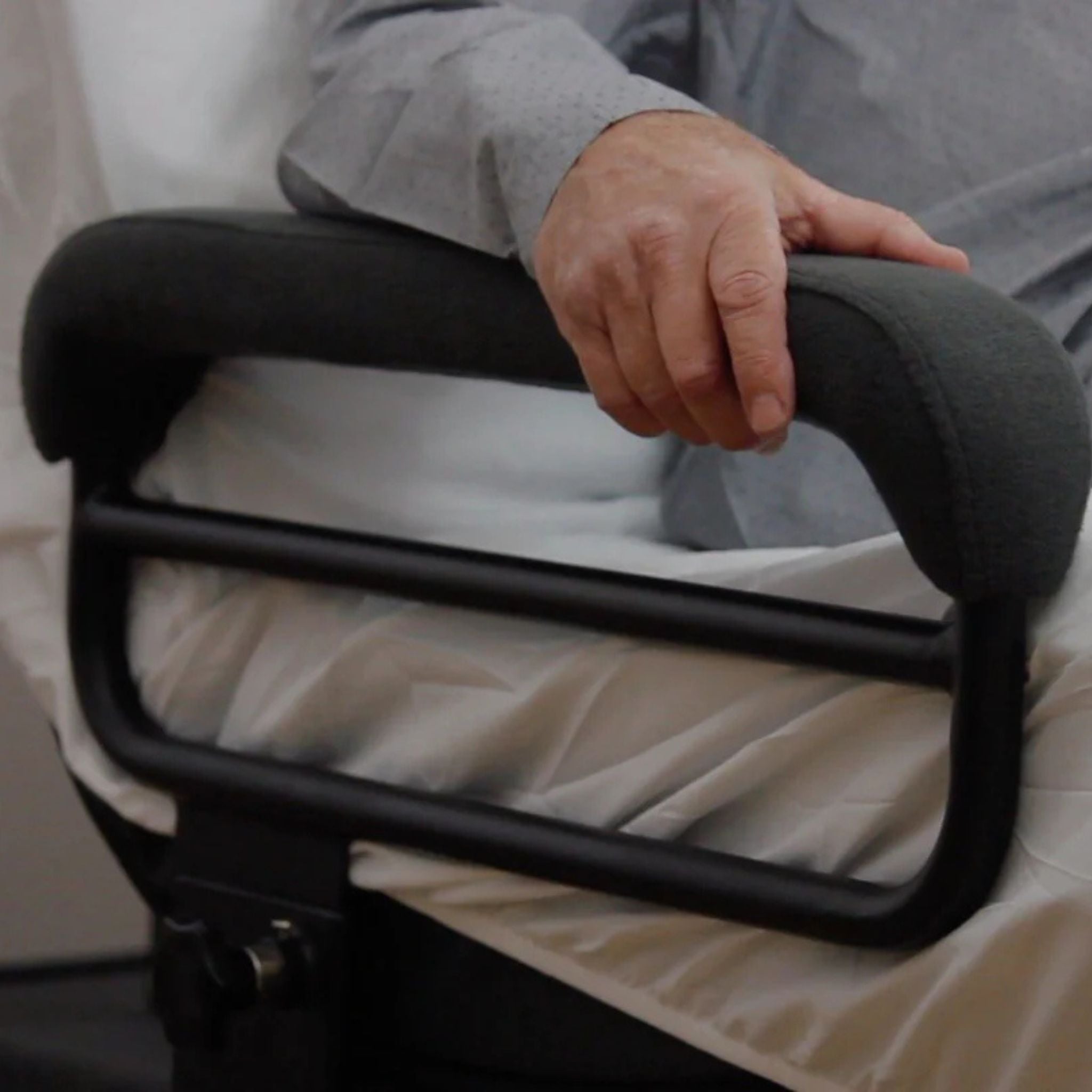 Close-up of a user gripping the padded side rail on the ENVYY Sleep-to-Stand adjustable bed by Platinum Health, highlighting supportive transfer assistance, user stability, and safer bed entry and exit.