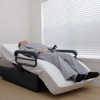 User resting comfortably in the ENVYY Sleep-to-Stand adjustable bed by Platinum Health with elevated head and leg positioning, padded safety rails, and remote-controlled comfort adjustments in a residential bedroom setting.