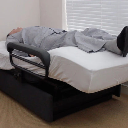 User lying comfortably in the ENVYY Sleep-to-Stand adjustable bed by Platinum Health with elevated leg positioning, supportive padded side rails, and ergonomic pressure-relief comfort in a residential homecare setting.