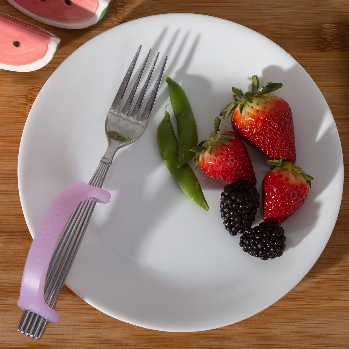 Lavender EaZyHold cuff on a fork beside a plate of strawberries, blackberries, and snap peas