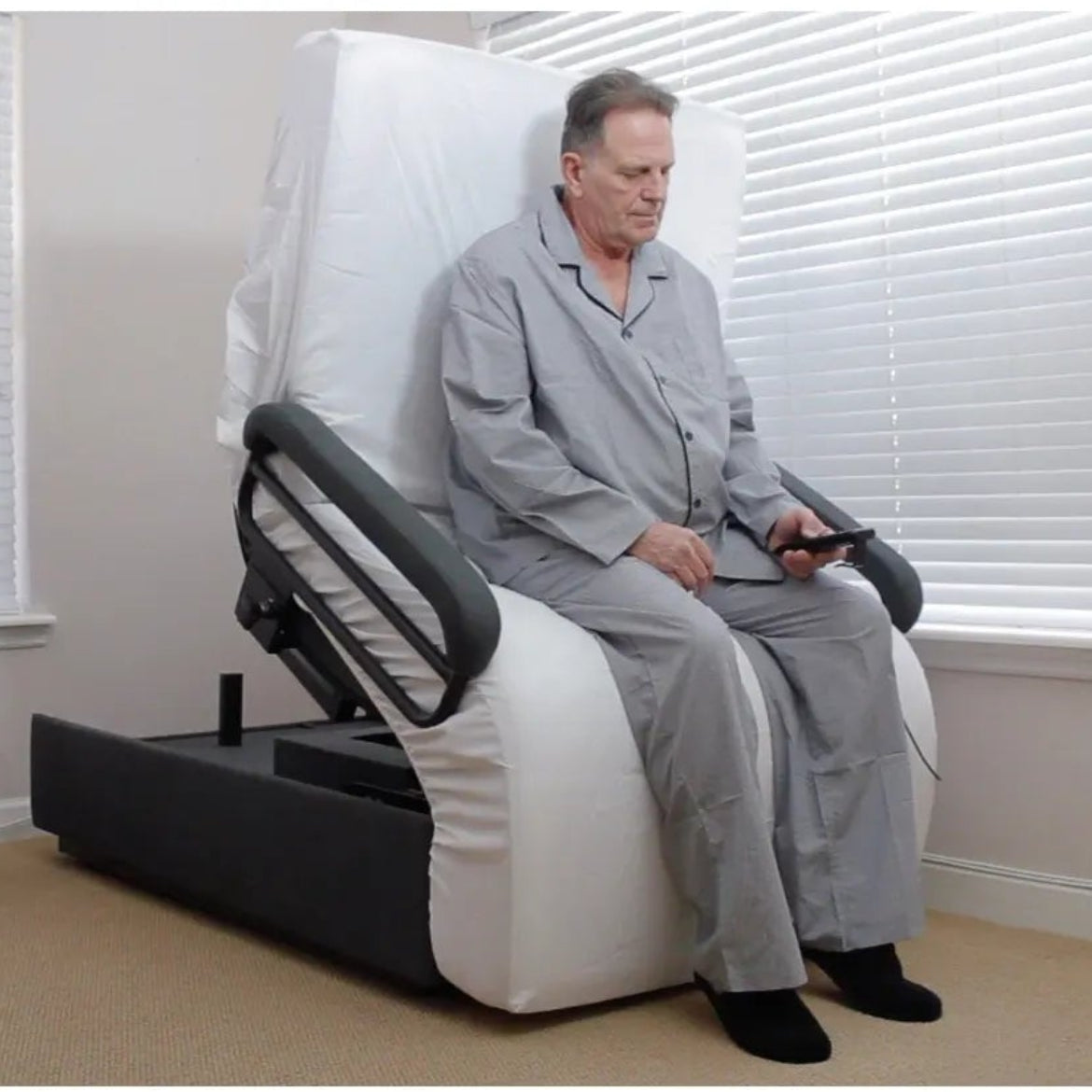 Man using an Envyy sleep-to-stand adjustable bed in an upright transfer position with padded side rails and powered standing assistance in a home bedroom.
