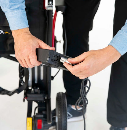 Hands connecting the charger cable to the charging port on the Feather Power Chair lithium battery