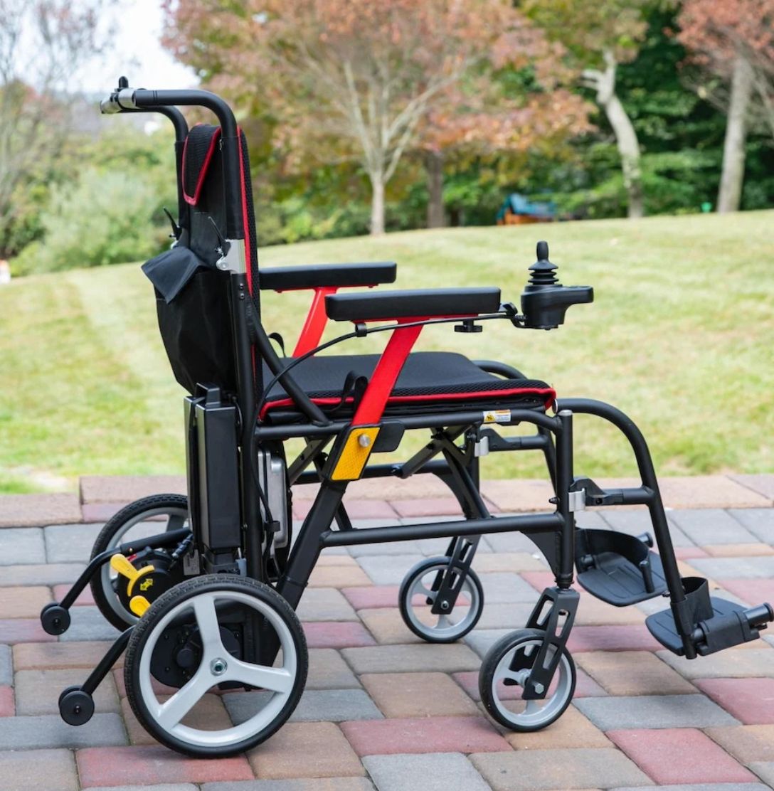 Side view of the Feather Power Chair on a brick patio showing anti-tippers, rear battery and joystick