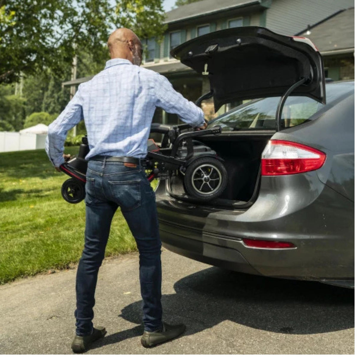 Man lifting the folded Feather Scooter into the trunk of a sedan in a driveway