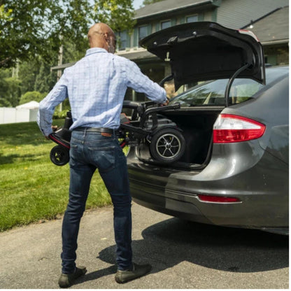Man lifting the folded Feather Scooter into the trunk of a sedan in a driveway