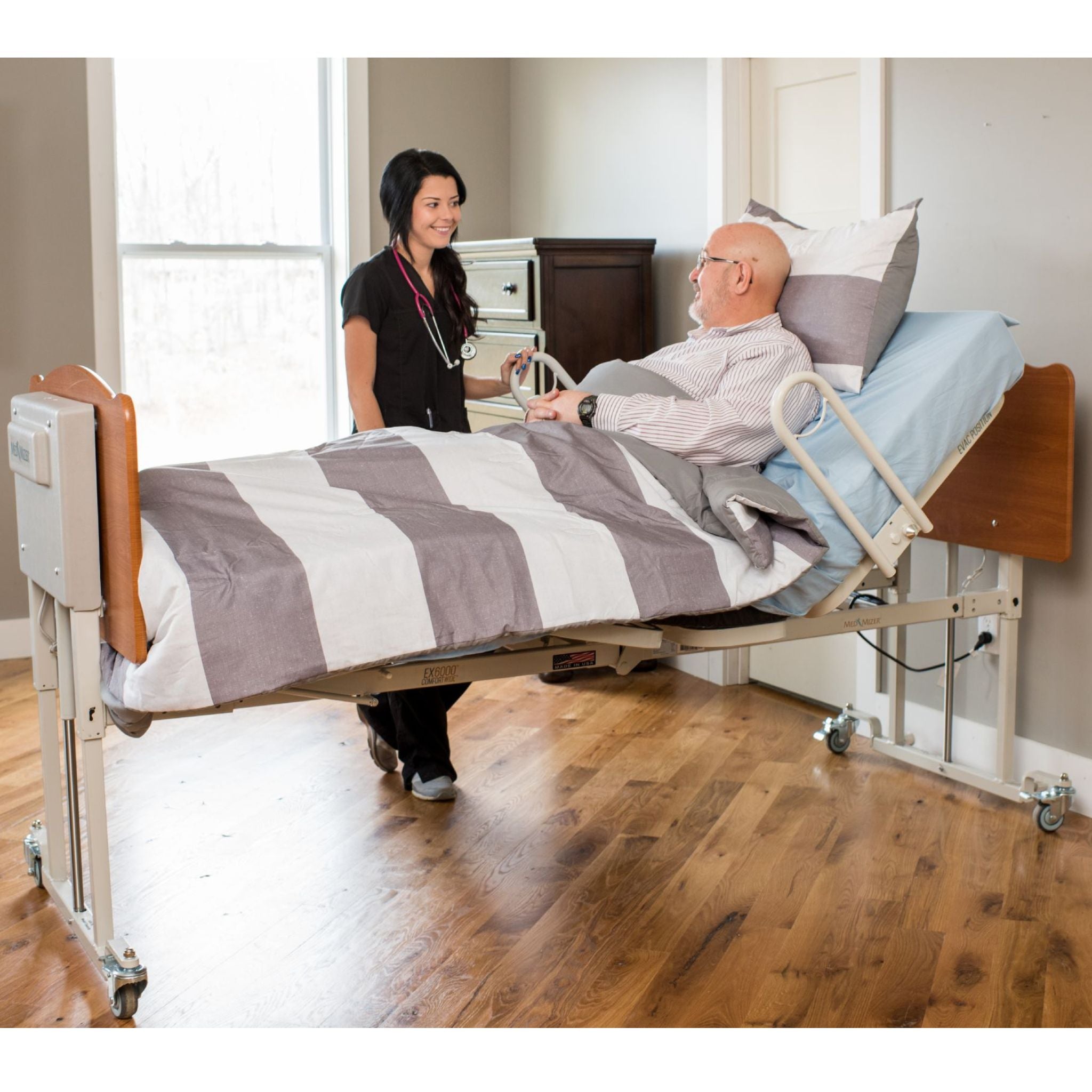 Caregiver assisting a seated patient in a Med-Mizer ComfortWide homecare bed in a home bedroom