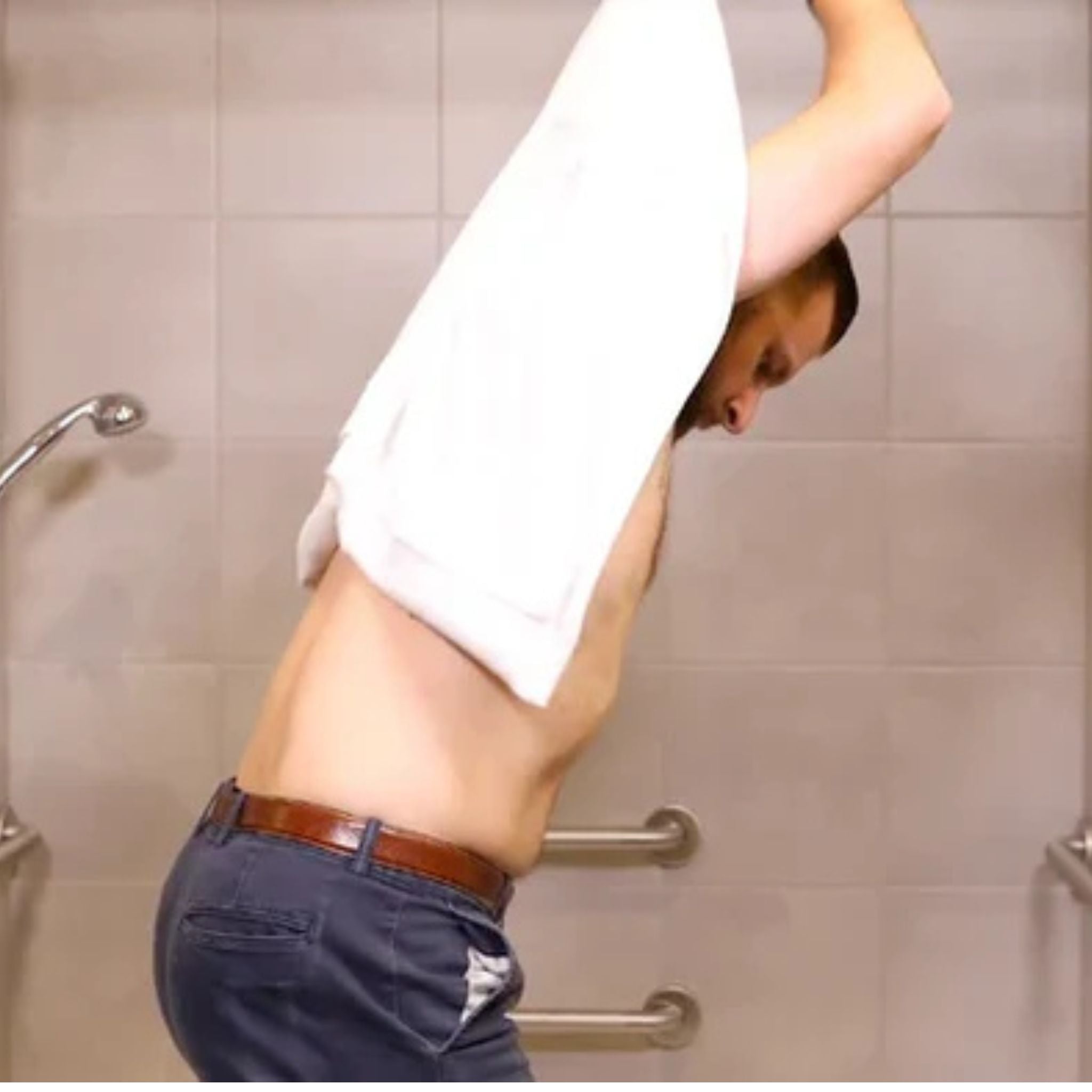 Man using the Mobility Towel by Kay Inspired while standing in an accessible shower to dry hard-to-reach areas with less bending and strain.