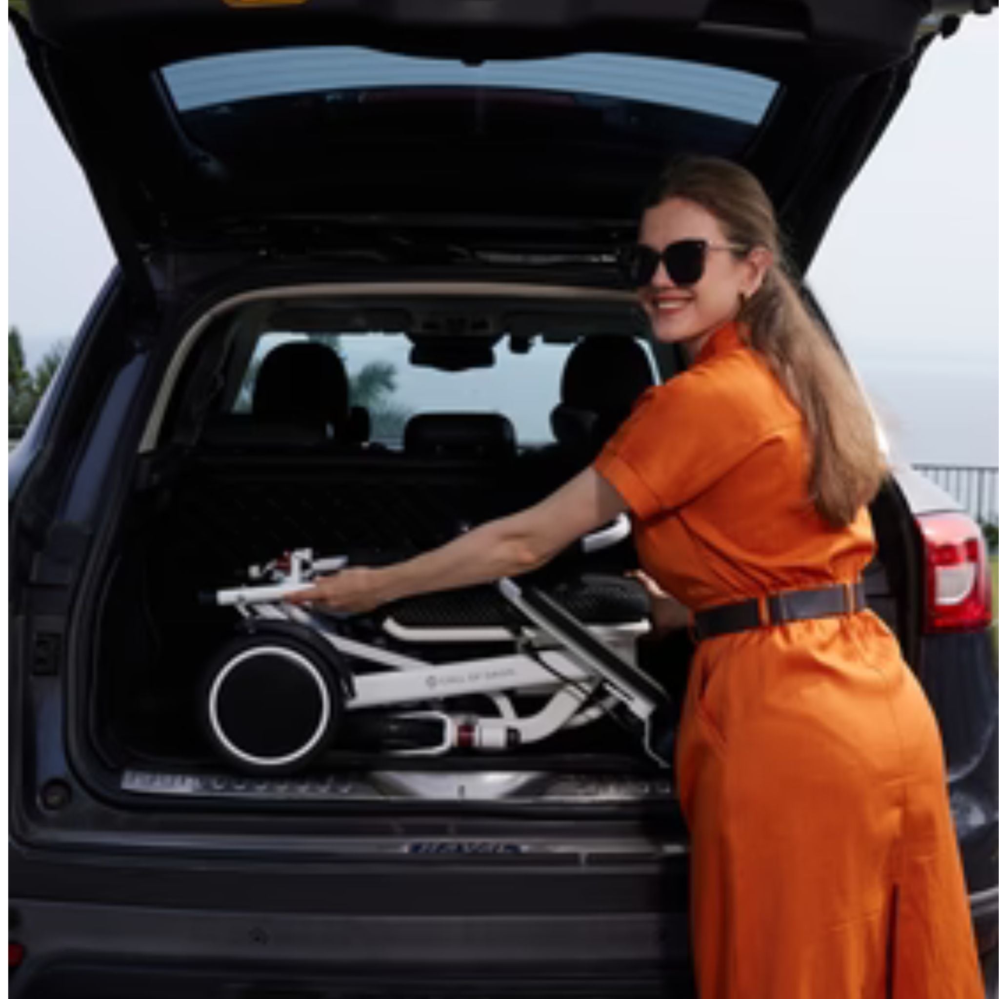 Person lifting the folded OAS Air Pro electric wheelchair into an SUV cargo area for transport