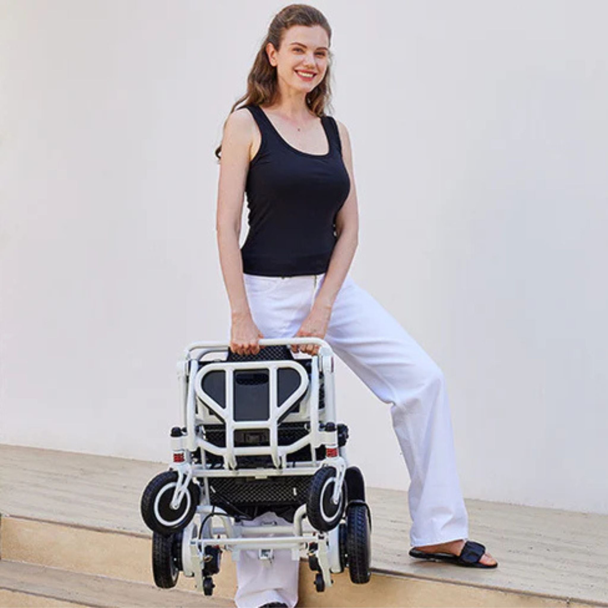 Person carrying the folded OAS Air Pro lightweight folding electric wheelchair by its integrated handle