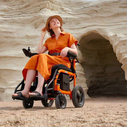 Woman relaxing in an orange OAS Air Ultra folding electric wheelchair on a sandy outdoor trail by rock formations