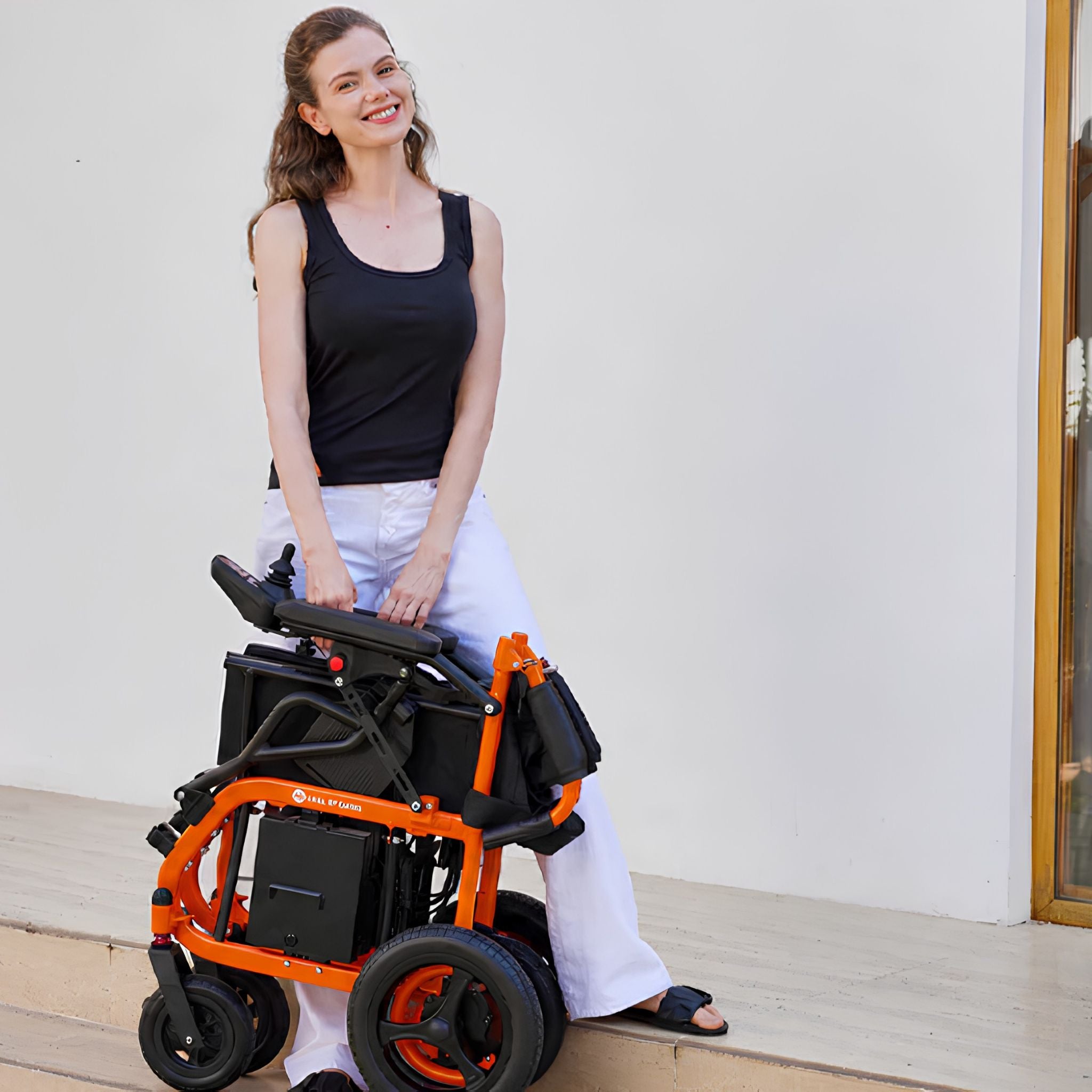 Woman easily lifting the folded lightweight orange OAS Air Ultra electric wheelchair by its frame outdoors