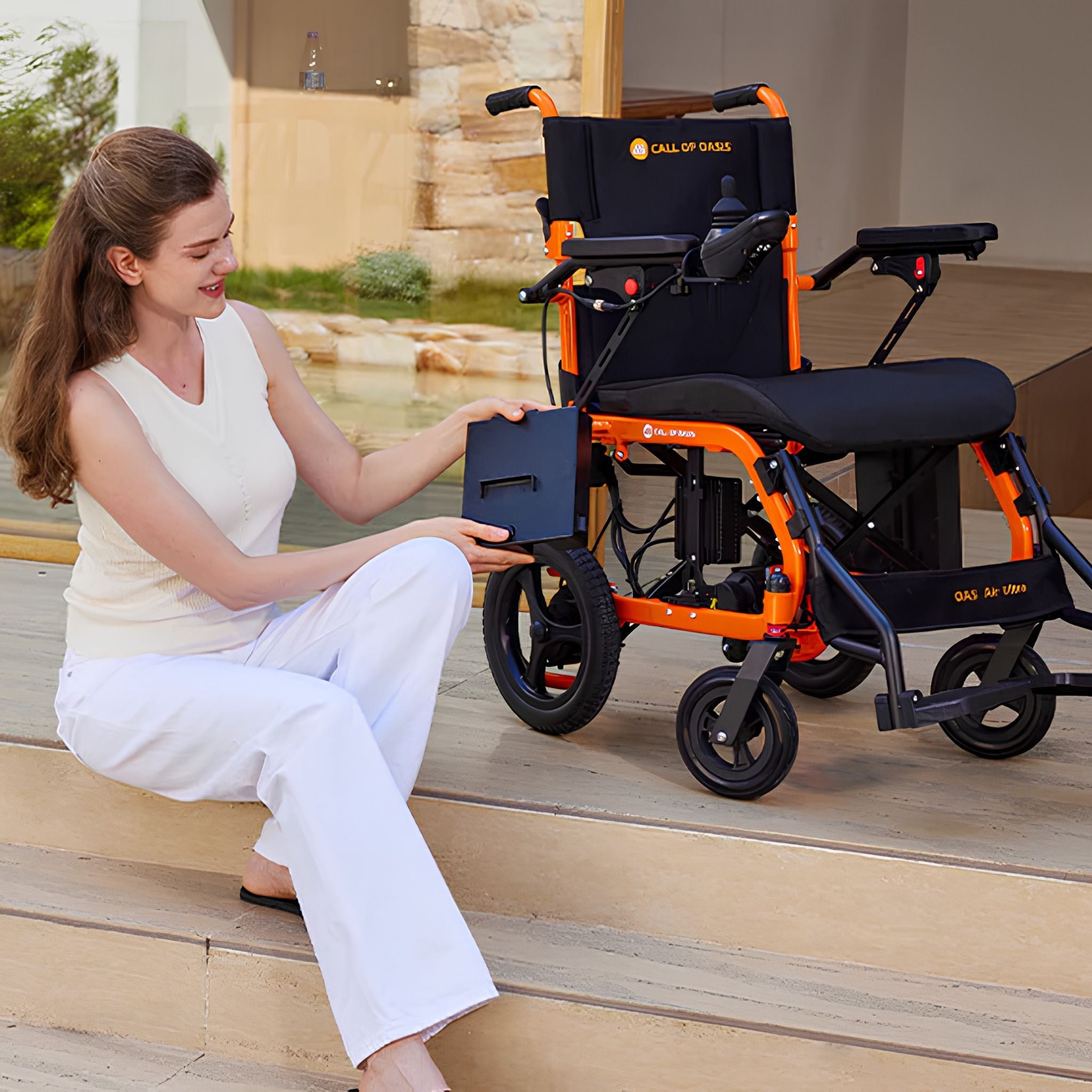 Woman lifting out the removable lithium battery pack from an orange OAS Air Ultra folding wheelchair outdoors