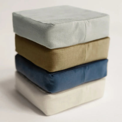 Tausi support cushions stacked to display available colors including blue, ivory and sand