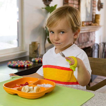 Young boy at a table using a yellow EaZyHold cuff to hold a spoon and feed himself fruit