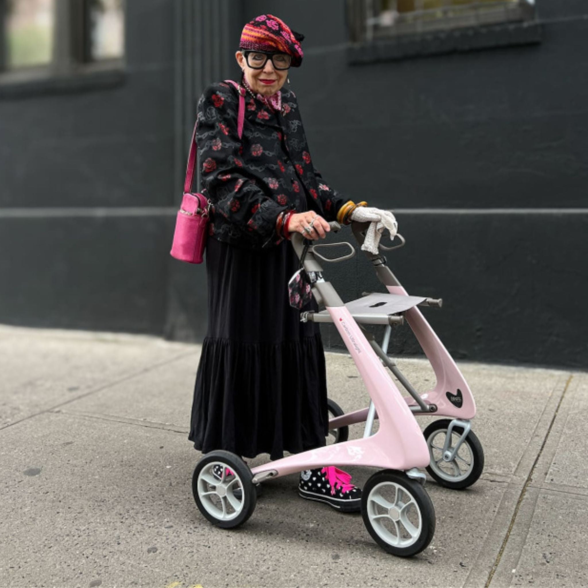 Woman standing with a Pale Rose byACRE Carbon Ultralight rollator on a city sidewalk