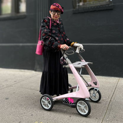 Woman standing with a Pale Rose byACRE Carbon Ultralight rollator on a city sidewalk