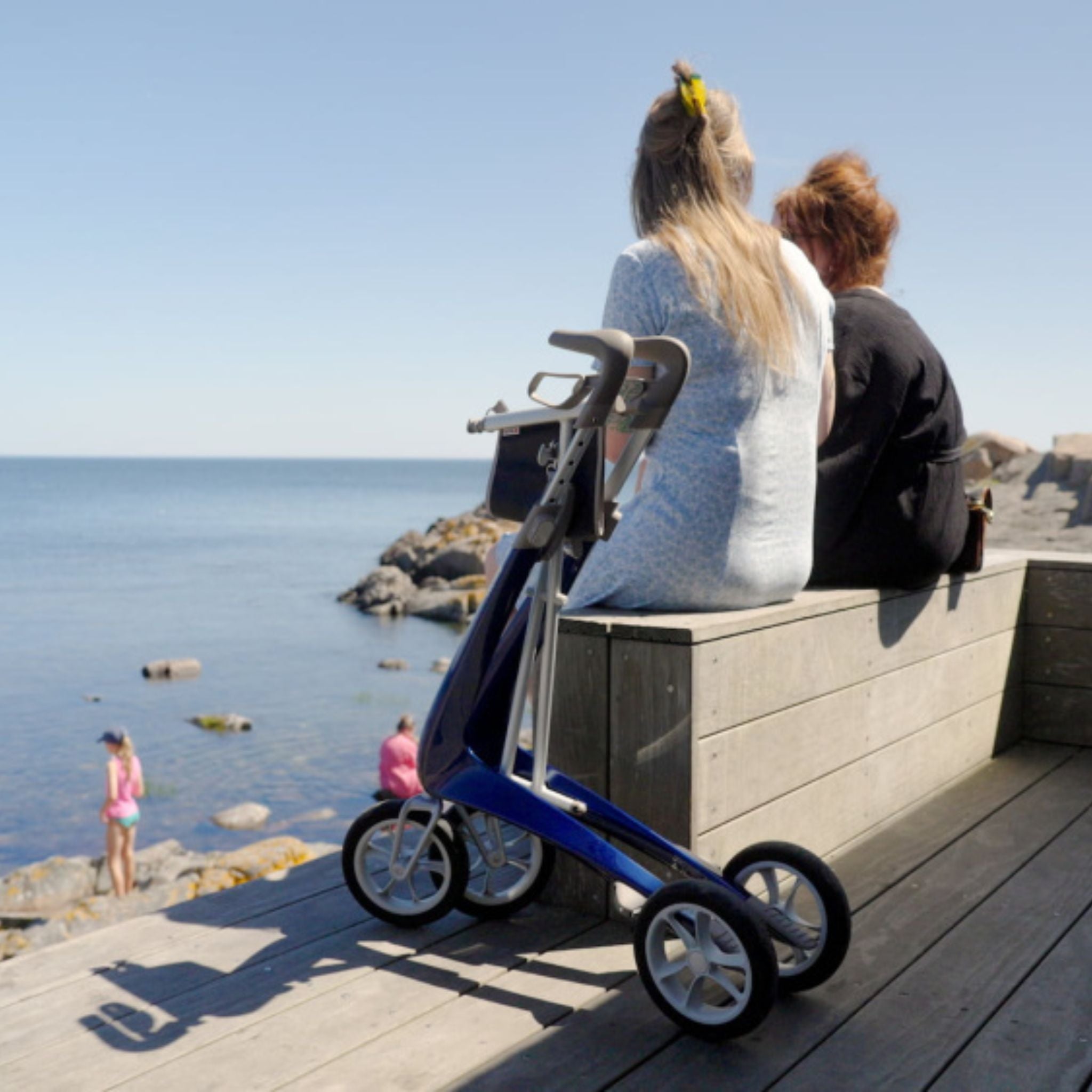Royal Blue byACRE Carbon Ultralight rollator parked beside two people on a seaside boardwalk