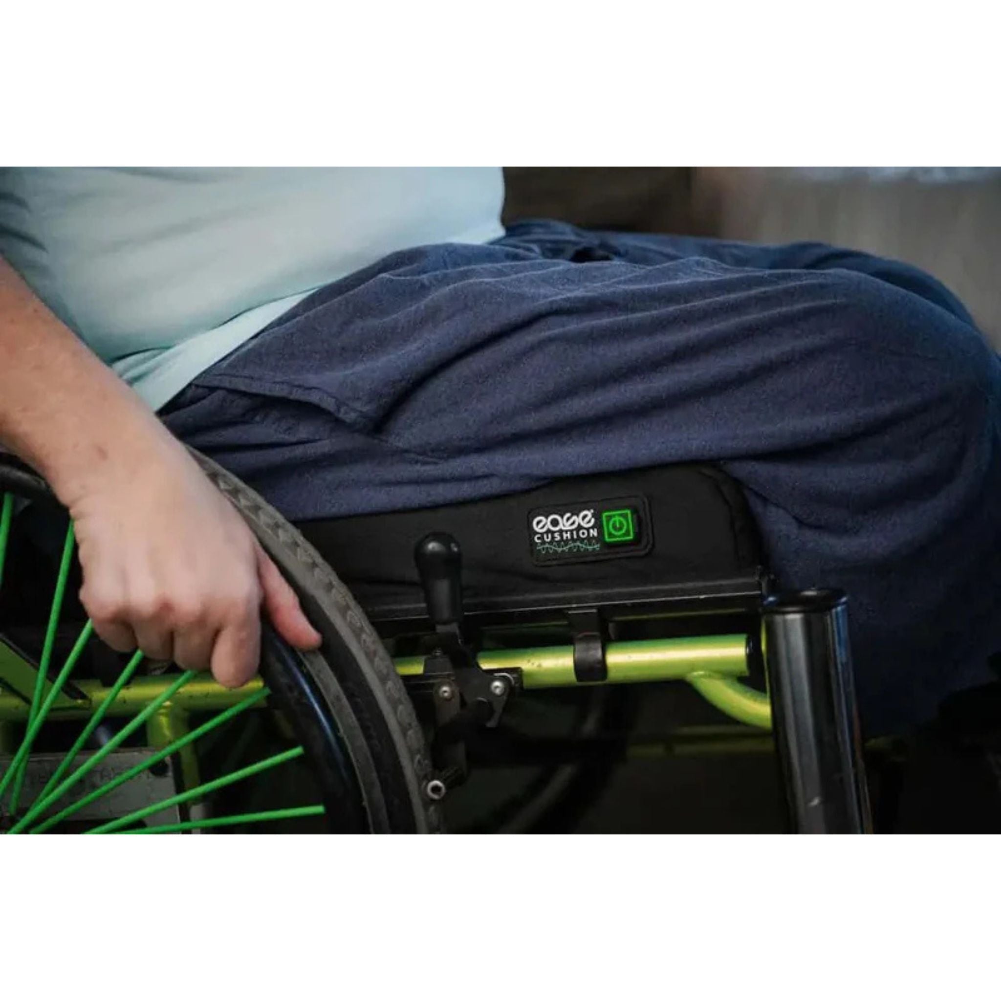 Man seated on an Ease Cushion smart wheelchair cushion, with the logo and green power button visible on the front edge