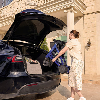 Woman lifting the folded Paiseec FLEX R3 in Blue into a car trunk beside groceries