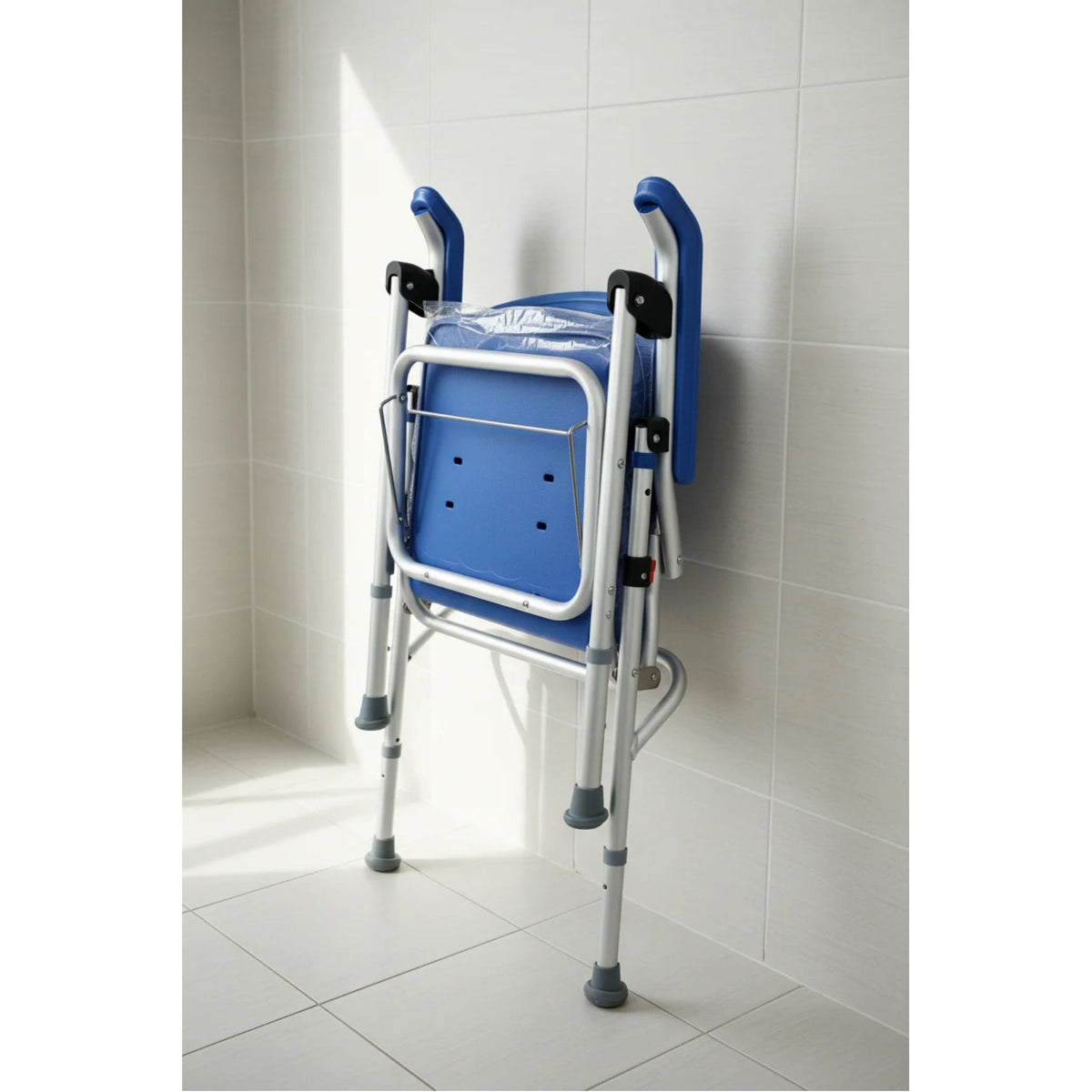 UltraCommode folded flat and leaning against a white tiled bathroom wall for compact storage